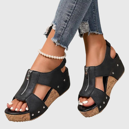 Black wedge sandals worn with ripped jeans on a light gray background