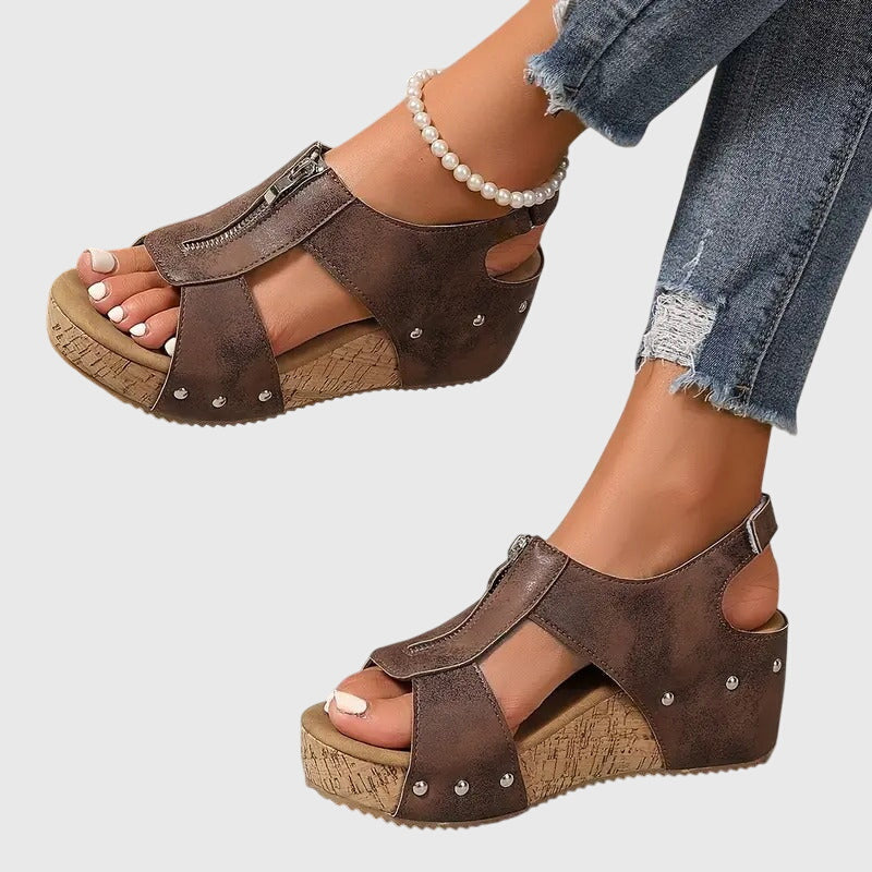 Brown open-toe sandals with cork wedge sole worn by a person on a light gray background