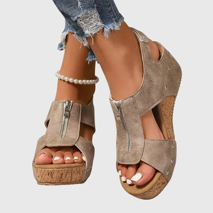 Beige suede sandals with cork platforms worn by a person on a light gray background