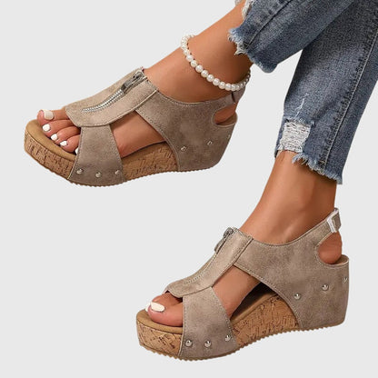 Beige wedge sandals worn with ripped jeans on a light gray background