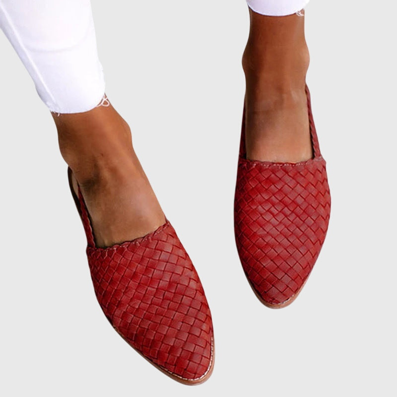 Red woven shoes worn with white pants on a light gray background