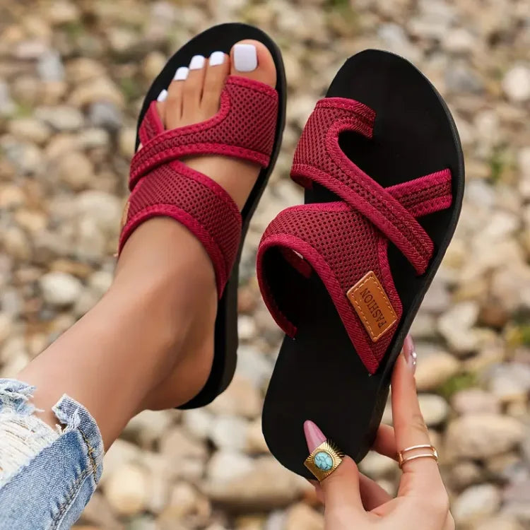 Red and black sandals with a brand logo held by a person against a rocky background
