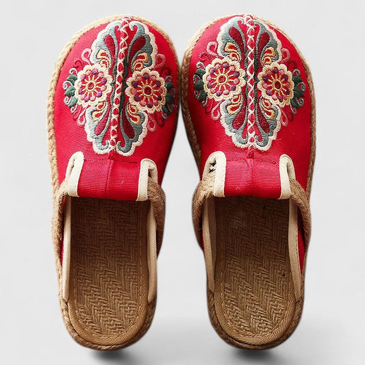 Pair of red embroidered slippers with brown soles on a light gray background