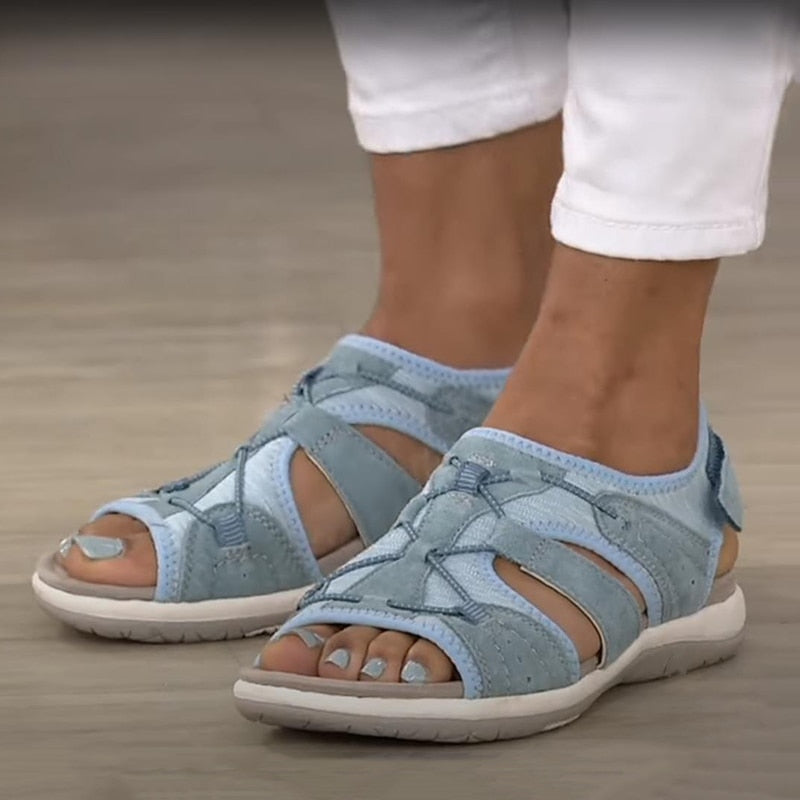 Blue sandals worn with white pants on a wooden floor