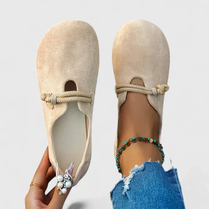 Beige flat shoes with rope detail worn by a person with blue jeans and a bracelet.