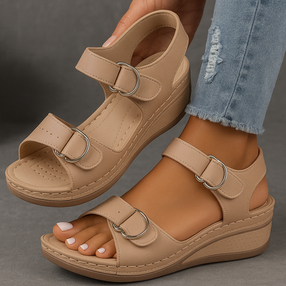 Beige wedge sandals with strap details worn by a person on a gray background