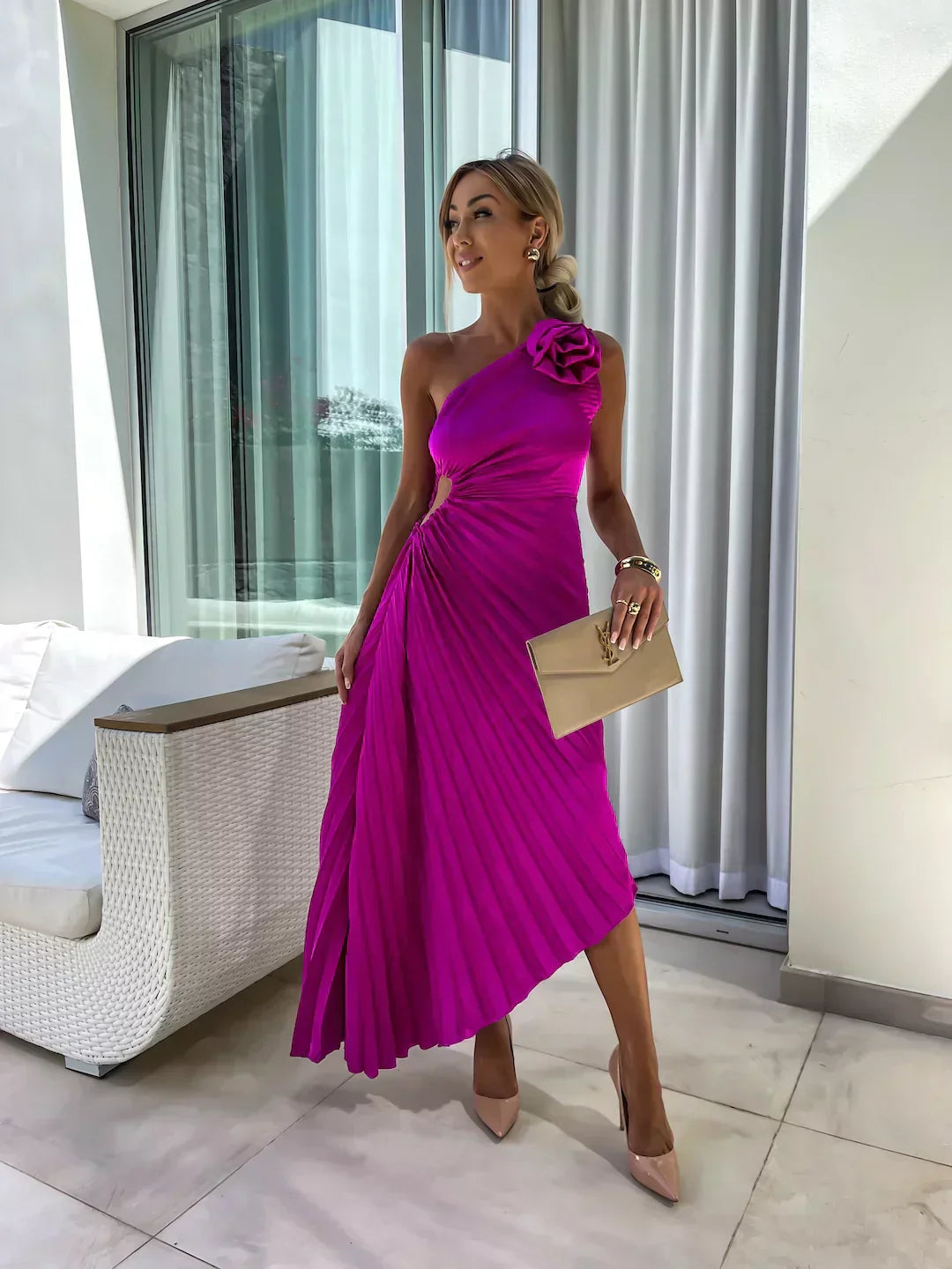 Woman in a vibrant pink dress with floral detail standing in a modern room.