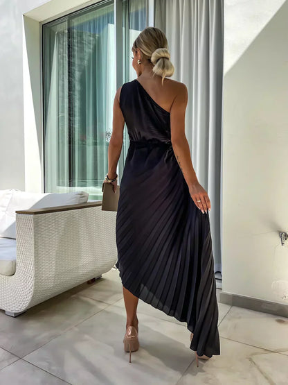 Woman in a black one-shoulder dress standing in a modern indoor setting.