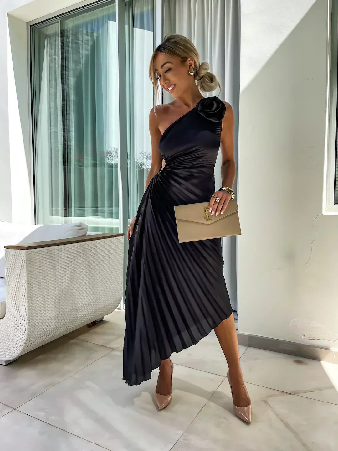 Woman in a black one-shoulder dress with a large flower detail, standing indoors.
