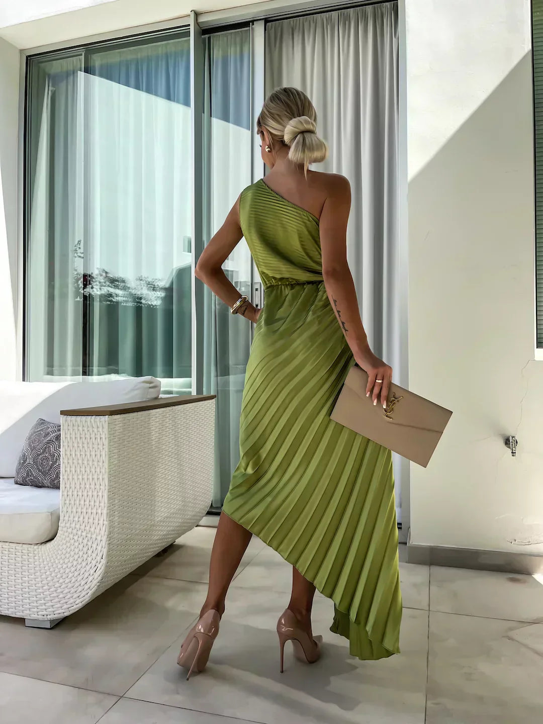 Woman in a green dress holding a beige clutch in a modern indoor setting.