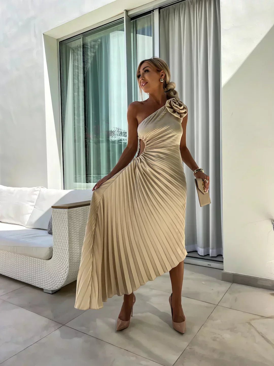 Woman in a beige pleated dress standing in a modern outdoor setting.