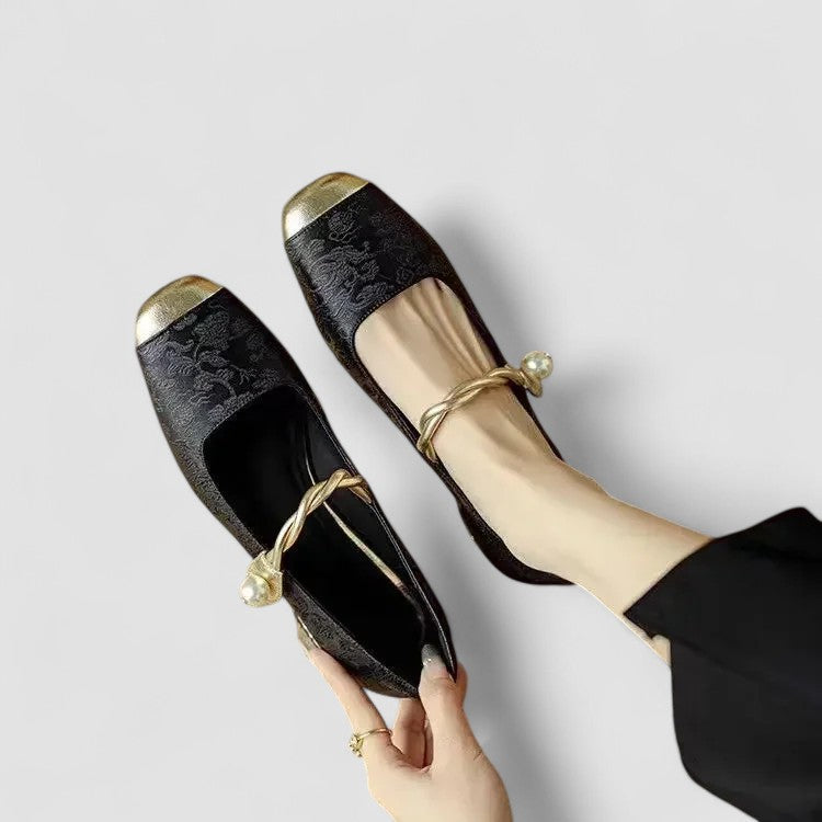 Black lace shoes with gold accents held by a hand on a light gray background