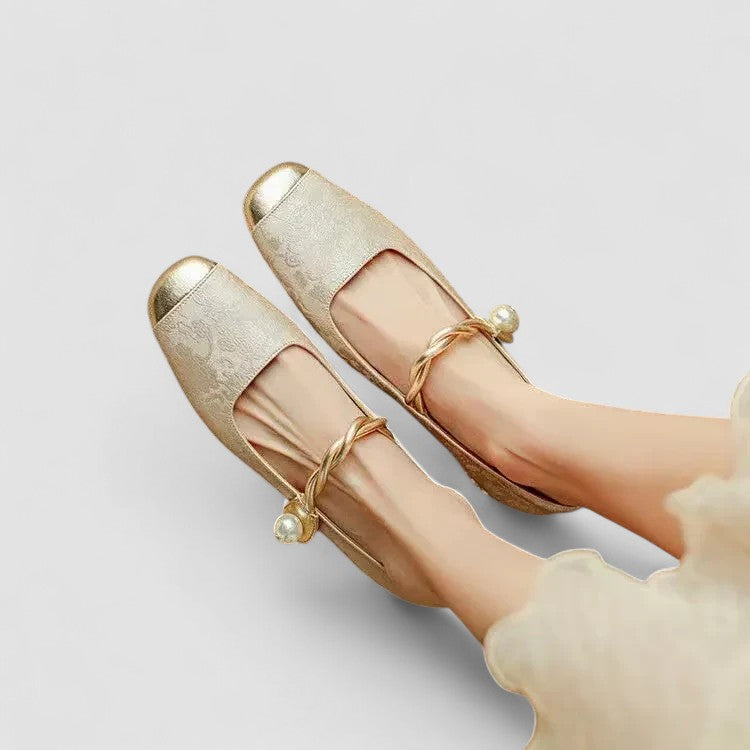 Pair of gold shoes with pearl accents on a light gray background