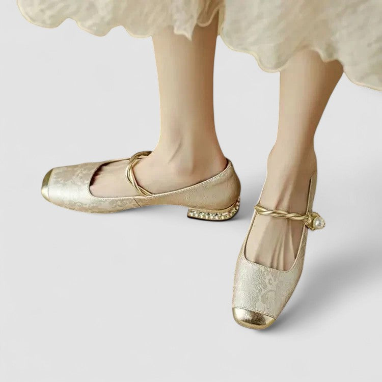 Gold ballet flats worn with a white lace dress on a light gray background