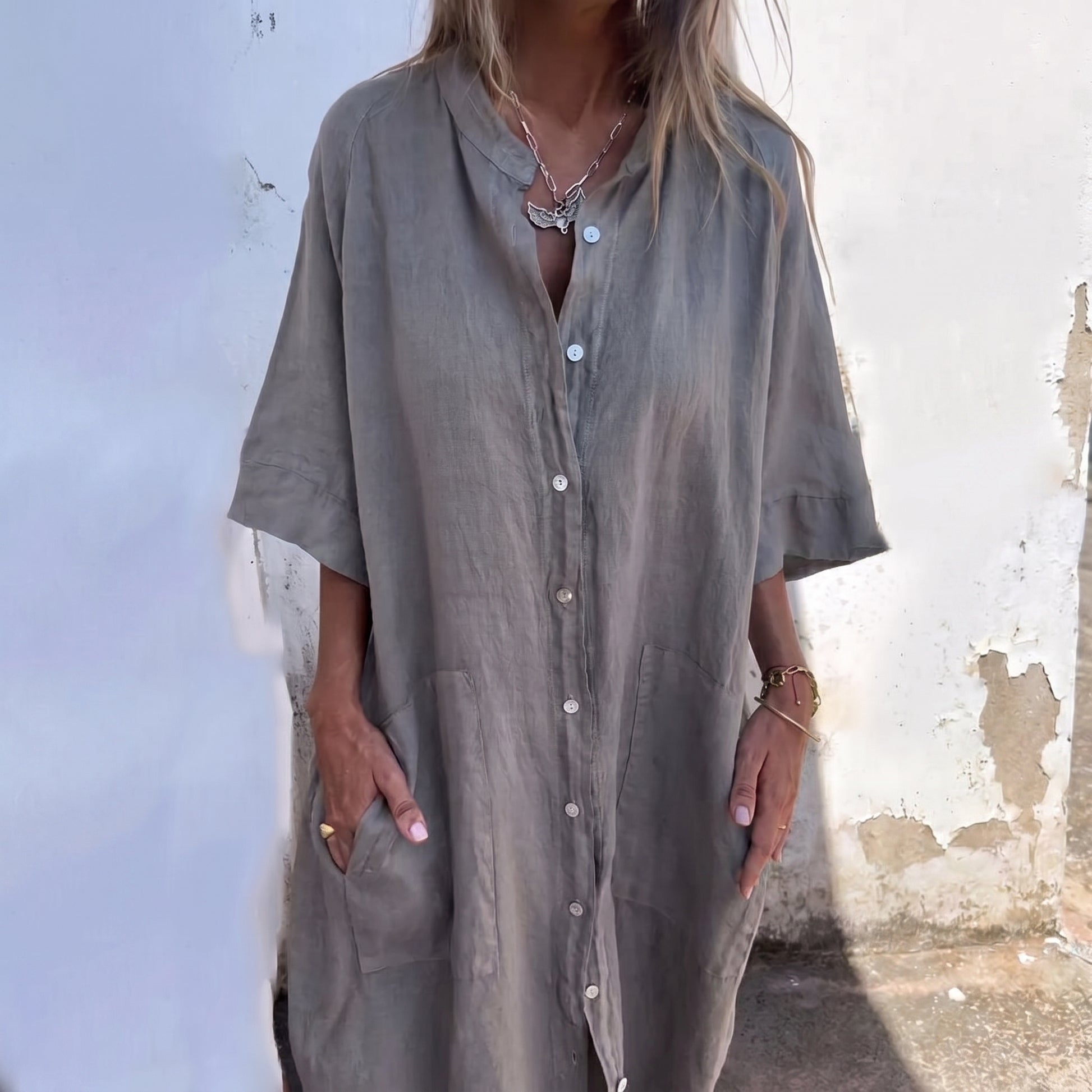 Person wearing a long, light-colored shirt against a textured wall.