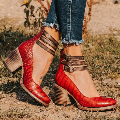 Red high-heeled shoes with brown straps worn outdoors on a grassy area.