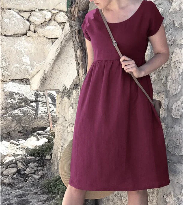 Woman wearing a burgundy dress standing against a stone wall.