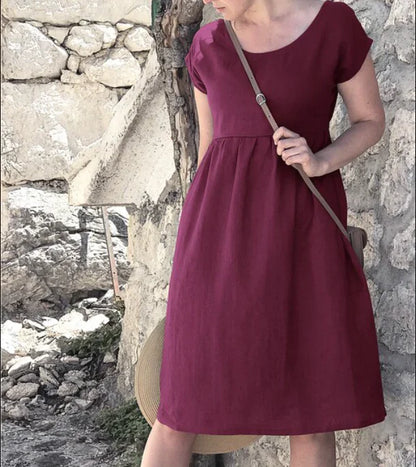 Woman wearing a burgundy dress standing against a stone wall.
