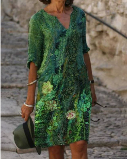 Person wearing a green floral dress standing against a stone wall.