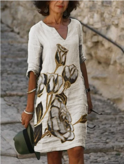 Woman wearing a white dress with floral design, standing on stone steps.