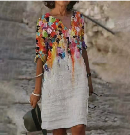 Woman wearing a colorful floral top over a white dress with a stone wall background