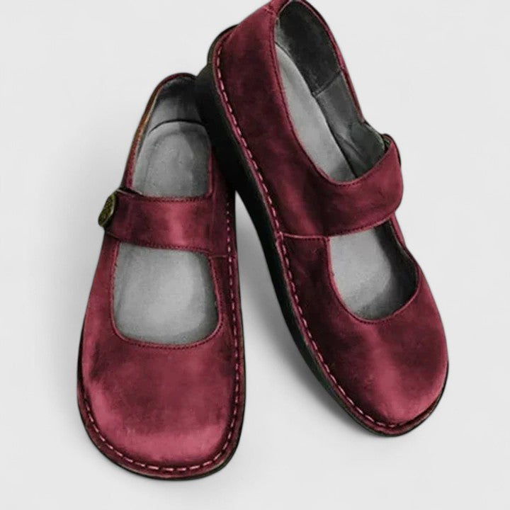 Pair of maroon children's shoes with a strap on a light gray background