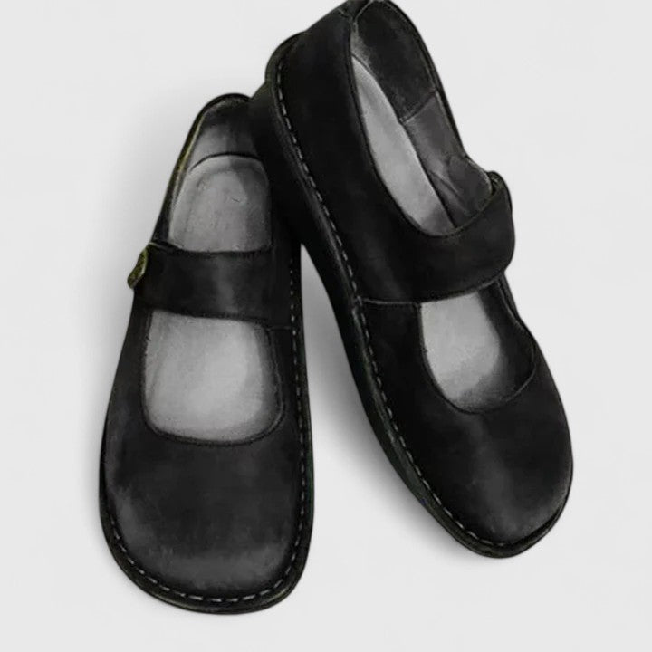 Pair of black leather shoes with a strap on a light gray background