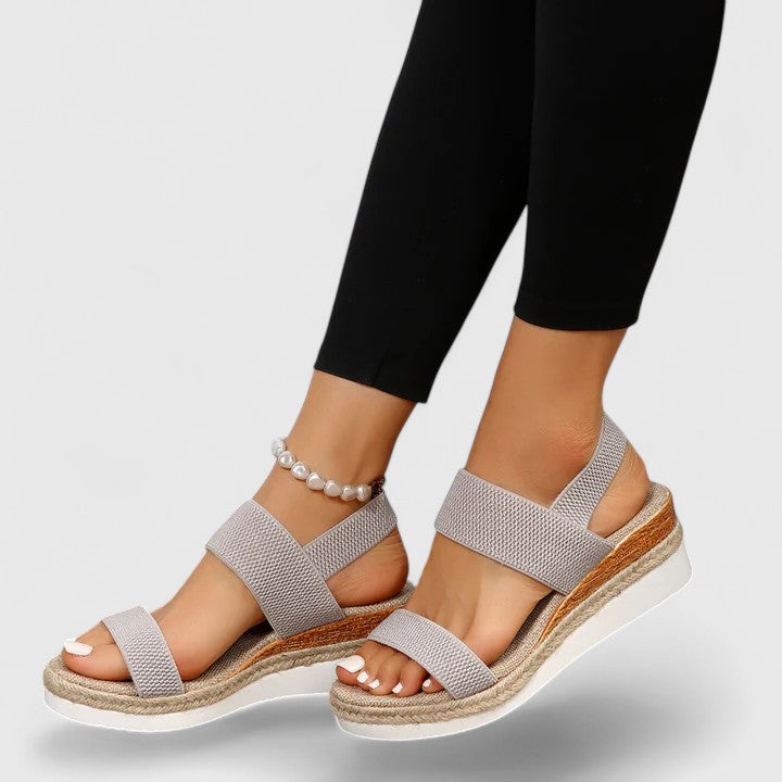 Gray sandals with wooden sole worn by a person on a light gray background