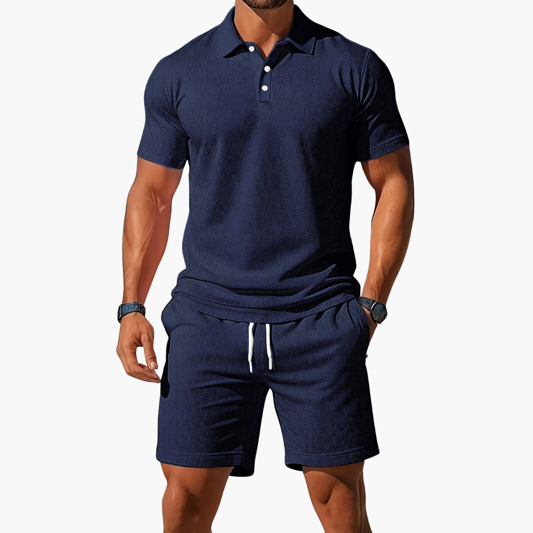 Man wearing a navy blue polo shirt and shorts set on a white background