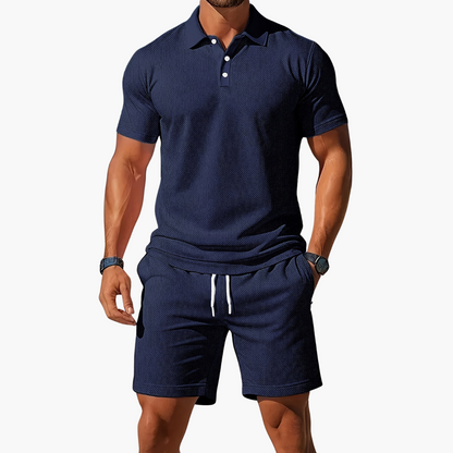 Man wearing a navy blue polo shirt and shorts set on a white background