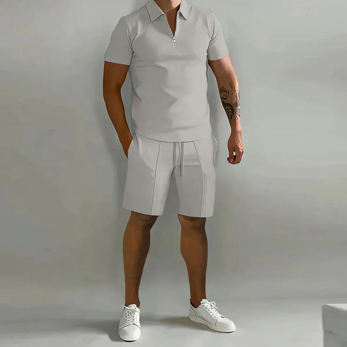 Person wearing a gray polo shirt and shorts set with white sneakers on a plain background