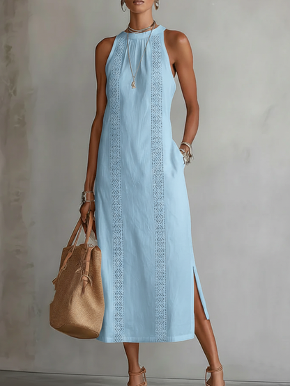 Woman wearing a light blue dress with intricate patterns, holding a brown handbag against a neutral background.