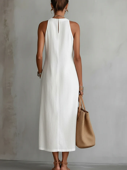 Woman wearing a white sleeveless dress holding a brown handbag against a gray background