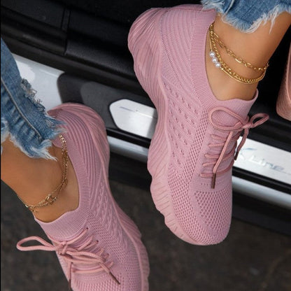Pink knit sneakers worn with denim jeans and gold jewelry, hanging out of a car window.