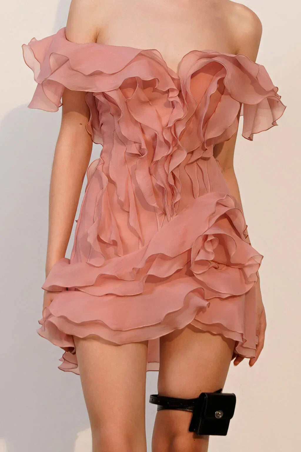 Pink ruffled dress on a mannequin against a plain background