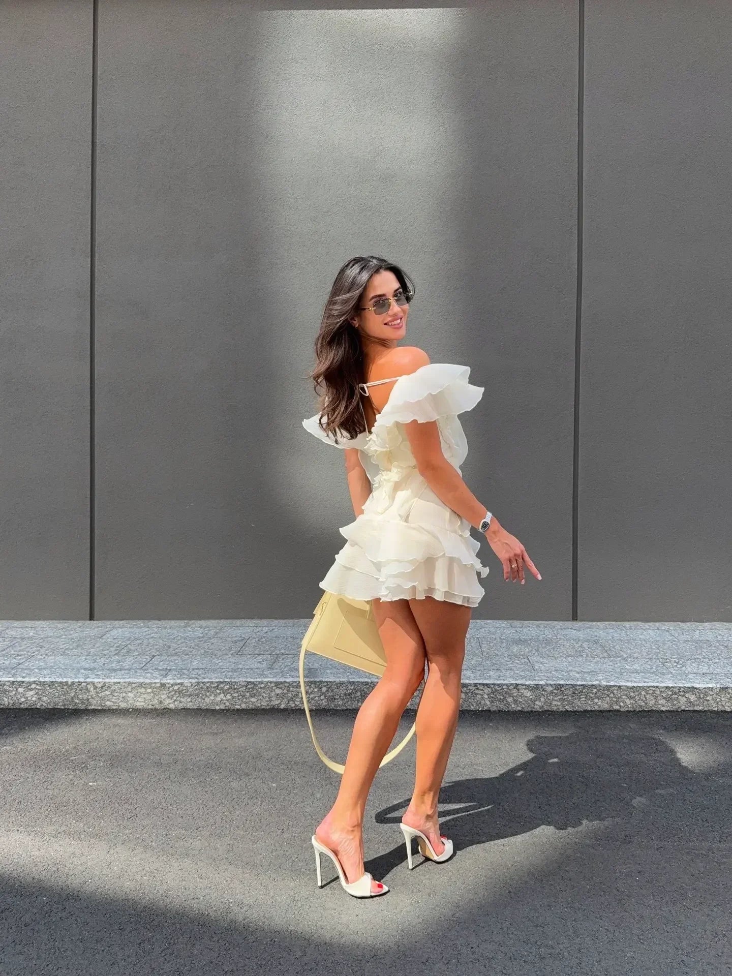 Woman in a white dress walking on a street with a gray wall in the background