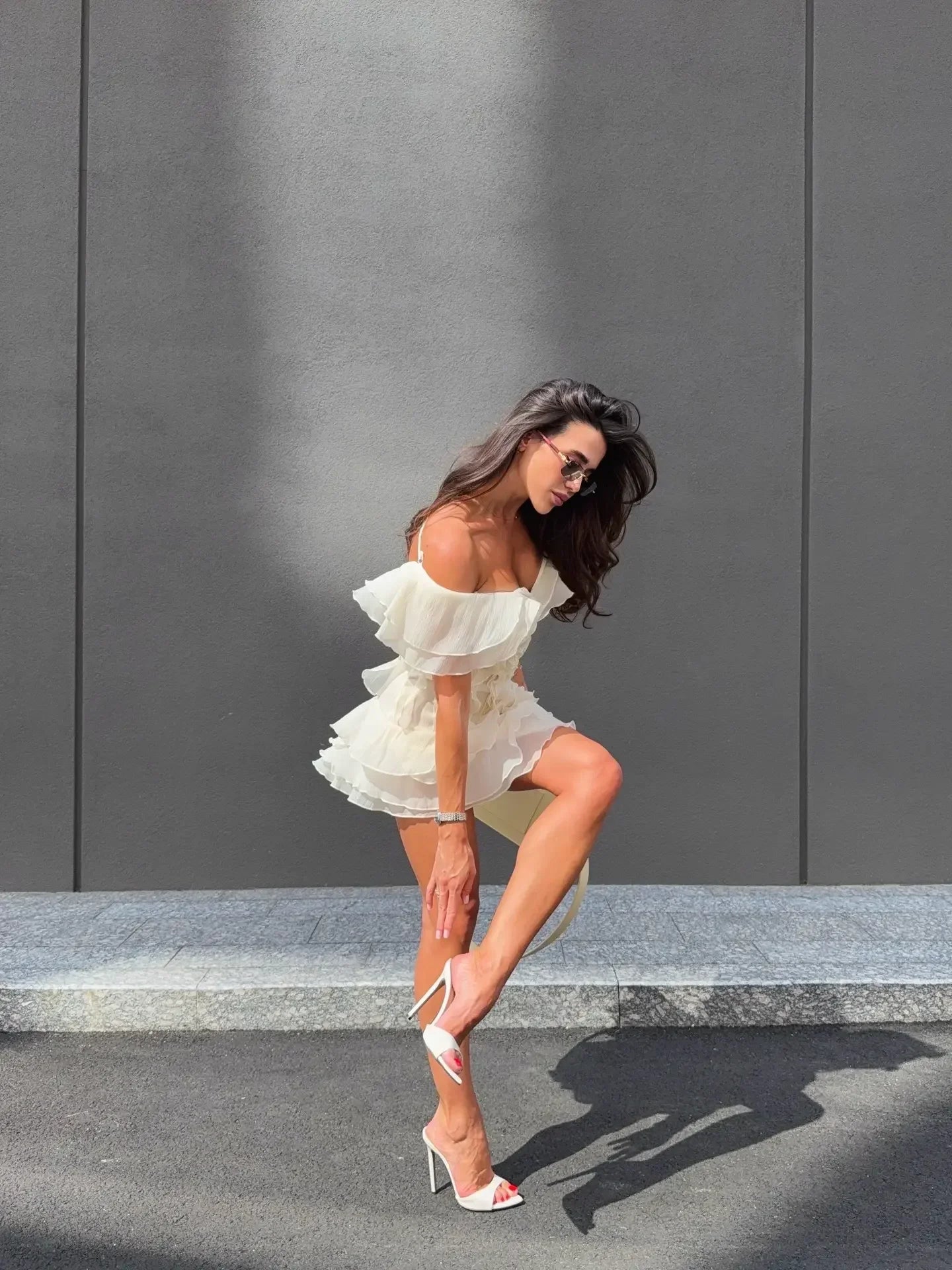 Woman in a white dress posing against a gray wall