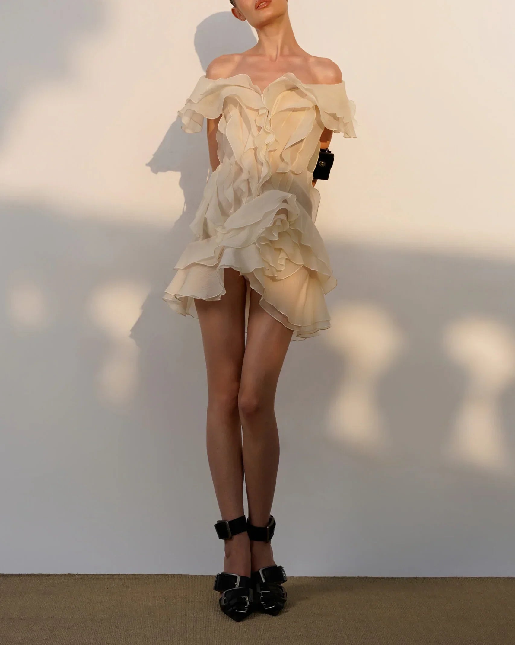 Woman wearing a beige off-shoulder dress with ruffled details against a plain background