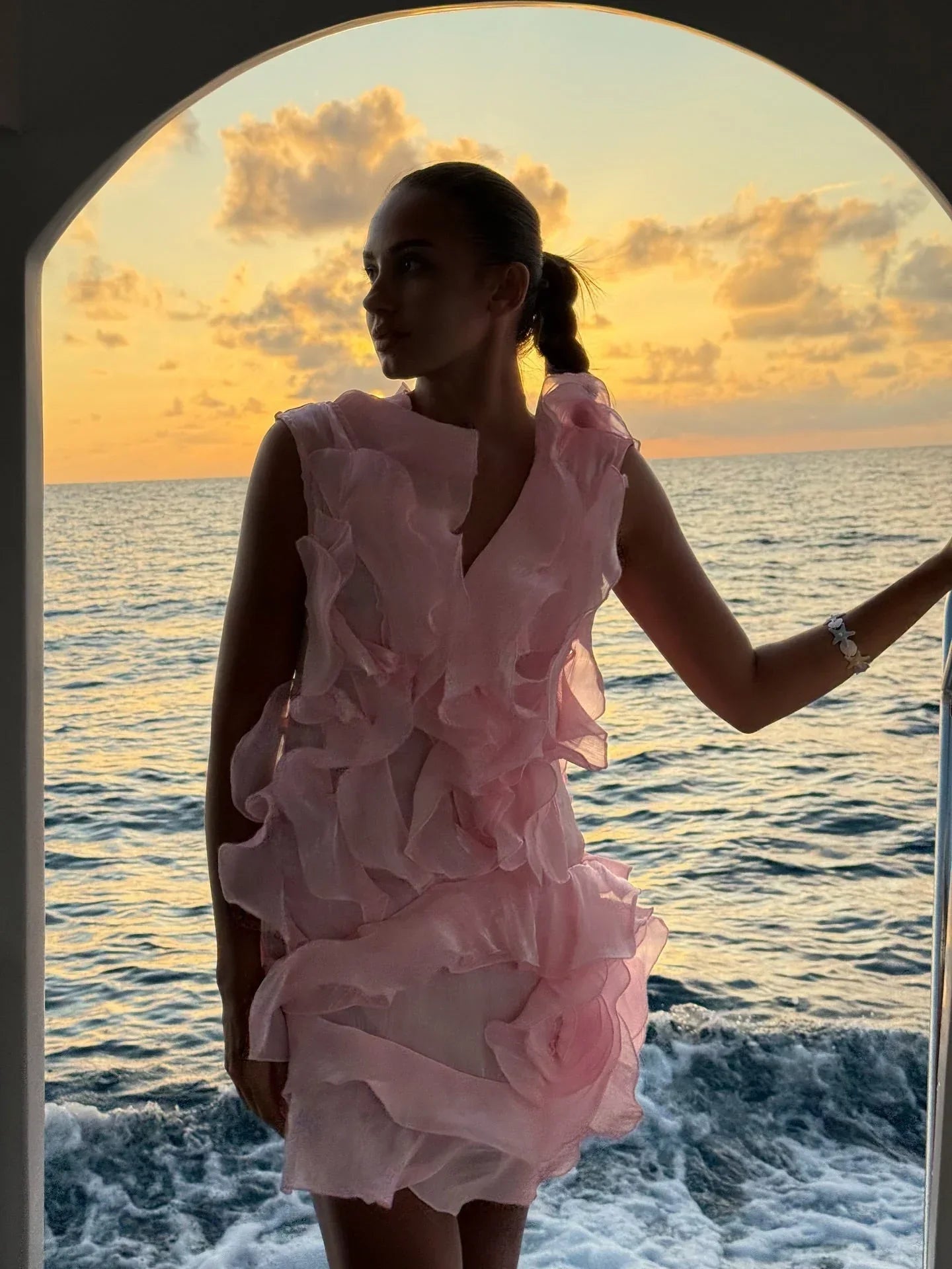 Woman in a pink dress standing by the ocean at sunset