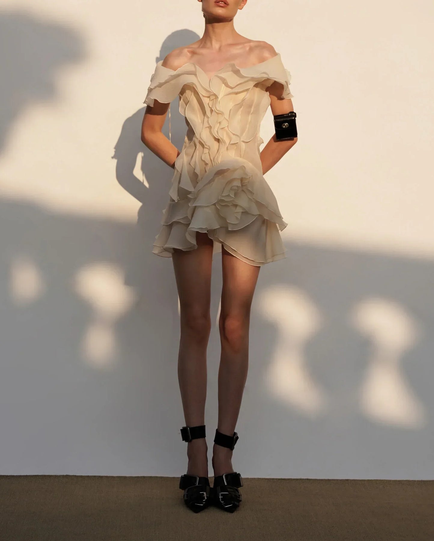 Woman wearing a beige off-shoulder dress with ruffled details against a neutral background