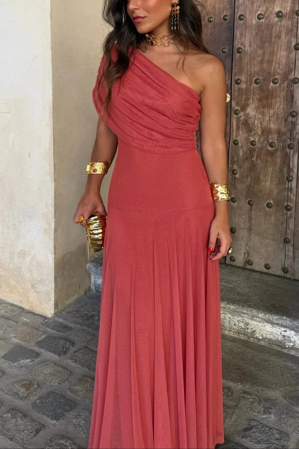 Woman in a coral one-shoulder dress standing in front of a wooden door.