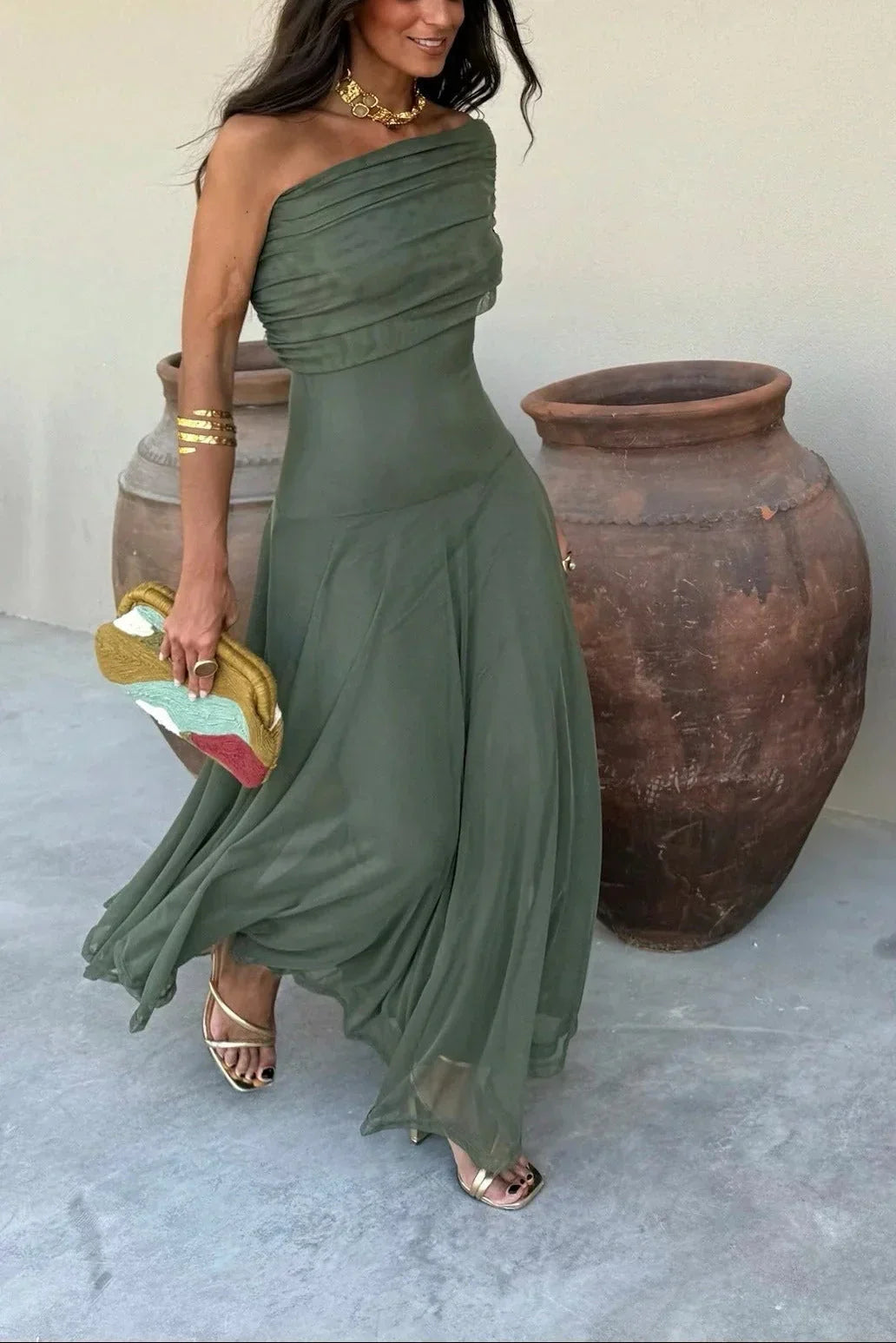 Woman in a green one-shoulder dress standing next to large pots.