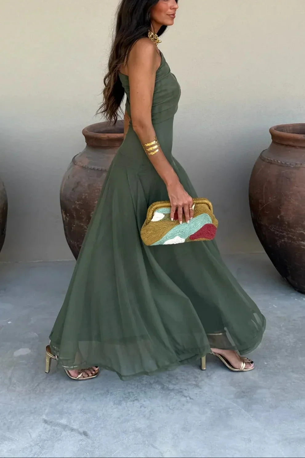 Woman in a green dress holding a colorful clutch against a neutral background