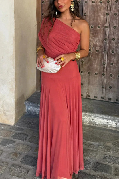 Woman in a coral one-shoulder dress standing in front of a wooden door.