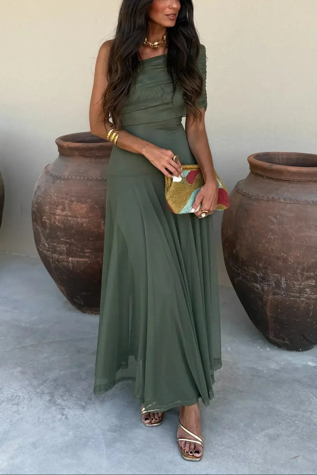 Woman in an olive green dress holding a clutch in front of large pots.
