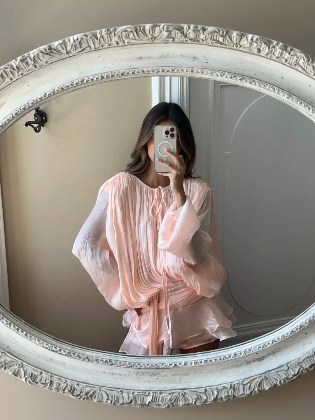 Person wearing a light pink dress in front of an ornate mirror.