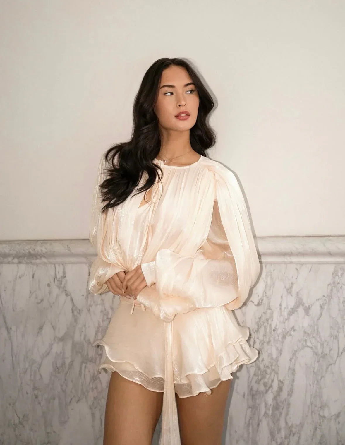 Woman wearing a light beige dress against a marble wall