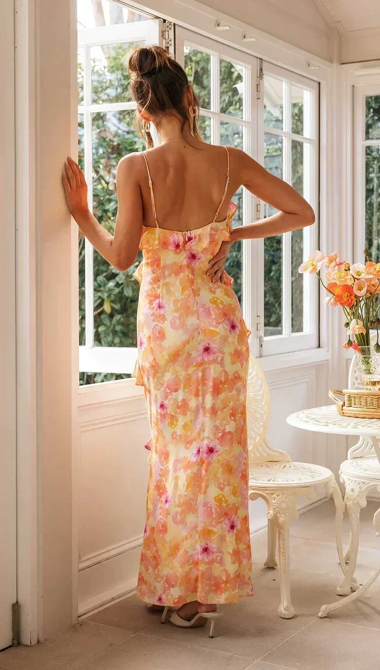 Woman in a floral dress standing in a sunlit room with large windows.