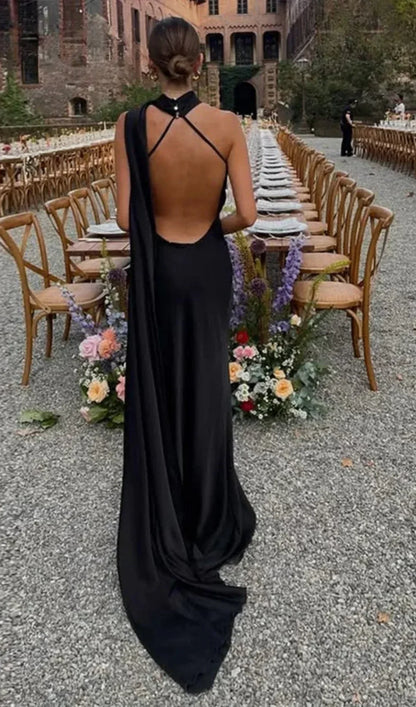 Woman in a black evening gown with an open back standing in front of a long table set for an event.