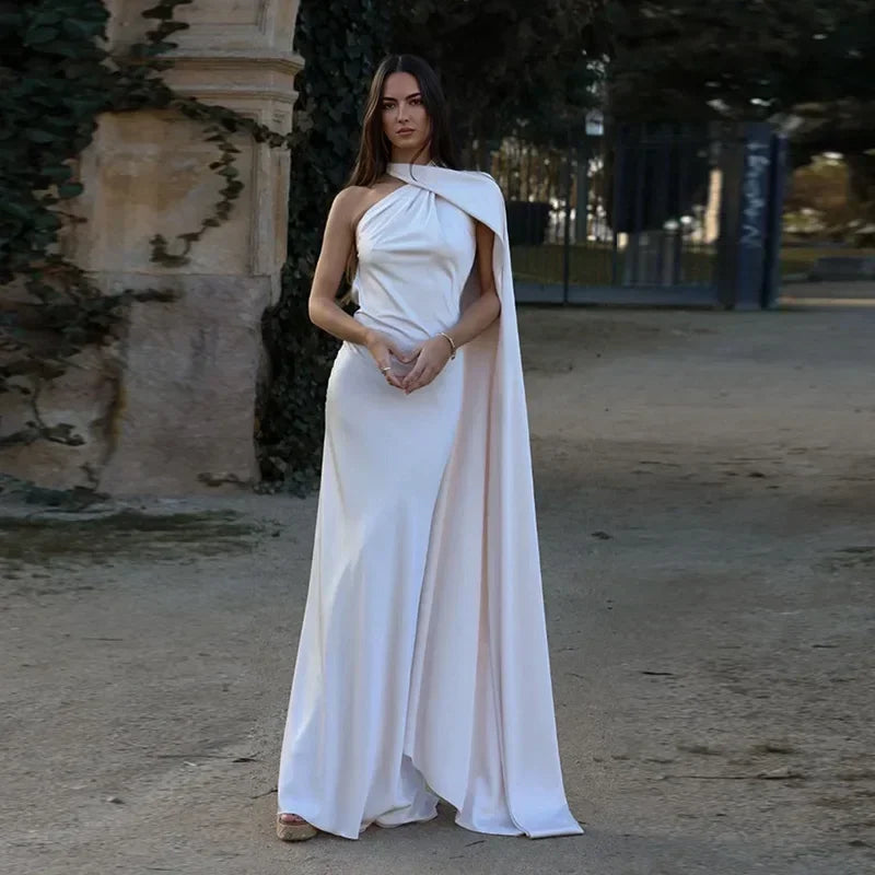 Woman in a white dress with a cape standing outdoors.